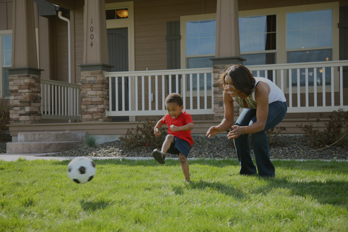 Family playing soccer outside of a new home.