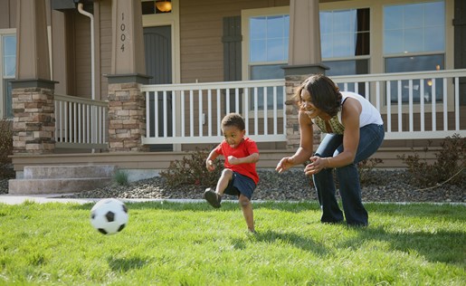 A mom and her son playing soccer in the front yard