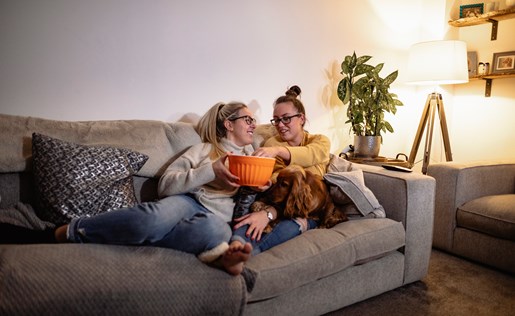 A couple eating popcorn on the couch with their dog