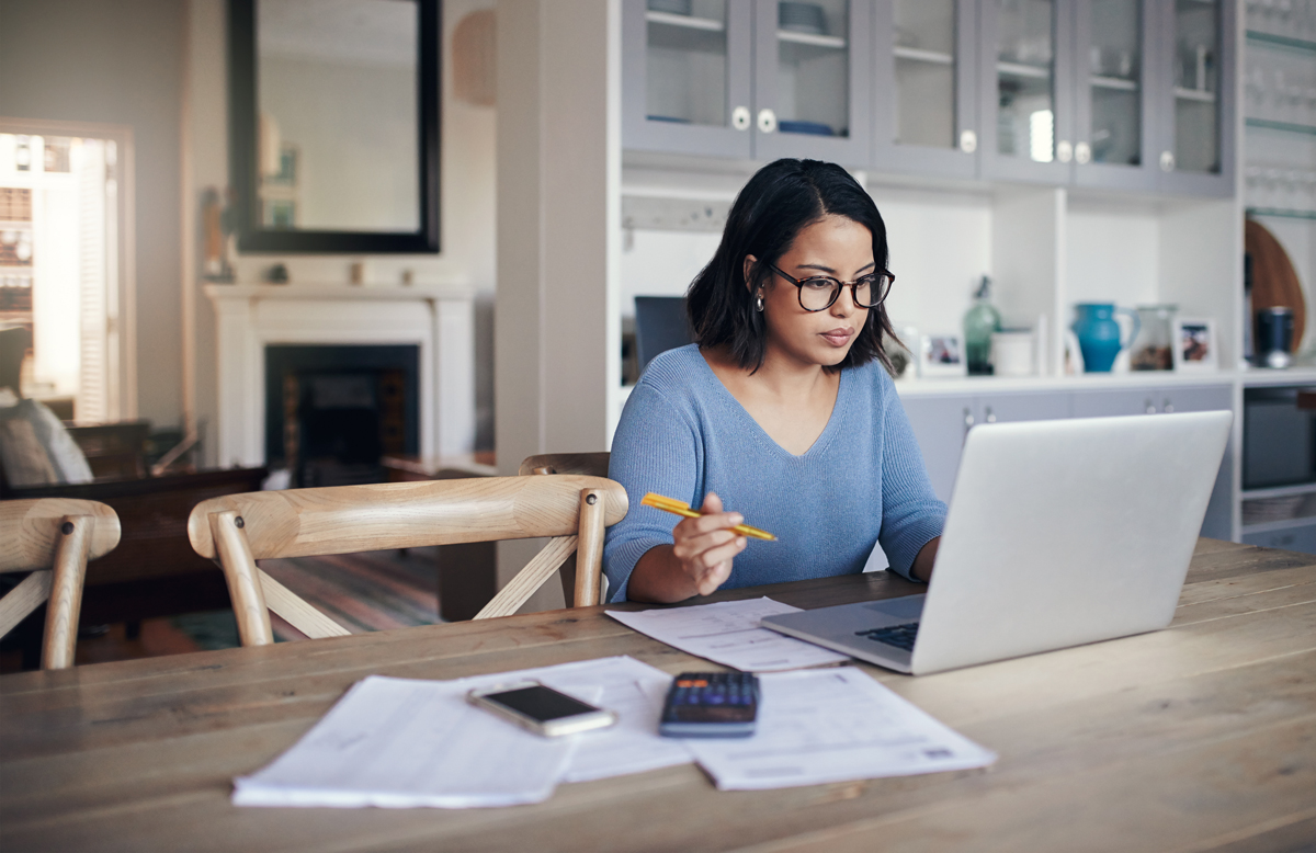 Woman working out her finances on her laptop in the kitchen.