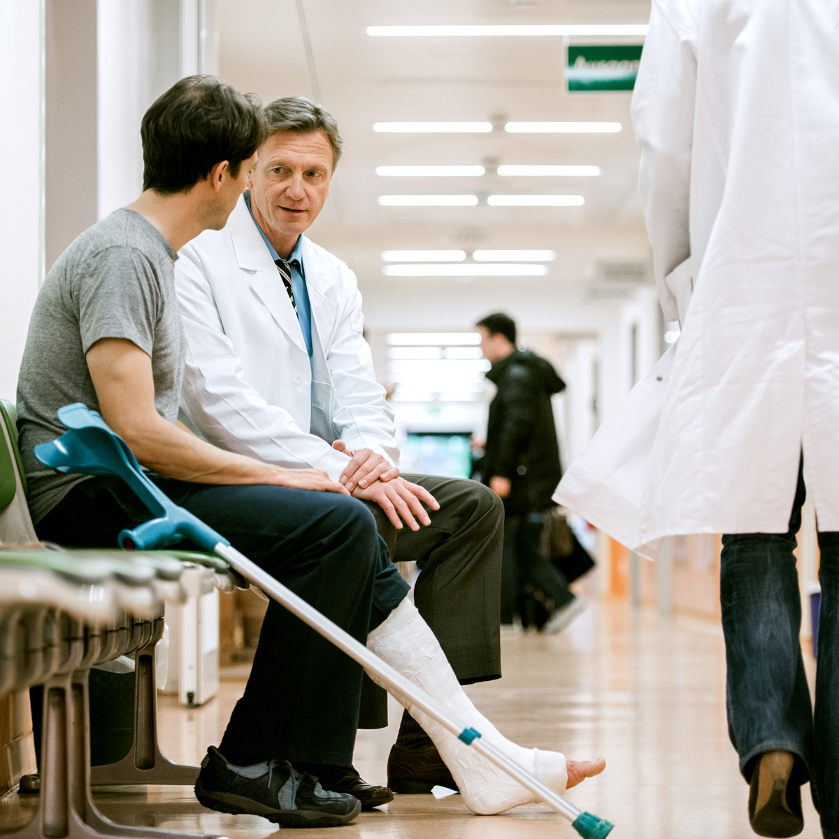 Man with crutches talking to doctor in hospital hallway.