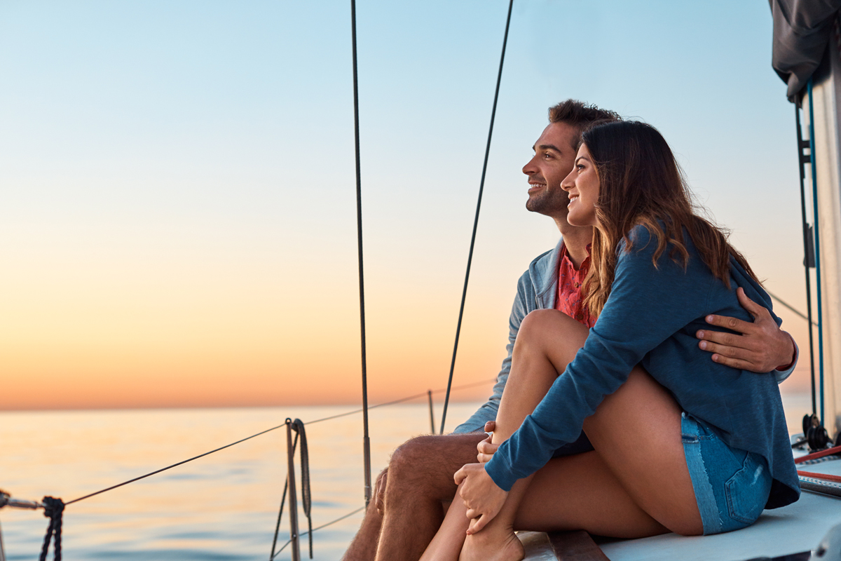 Couple hugging, watching a sunset on their sailboat.