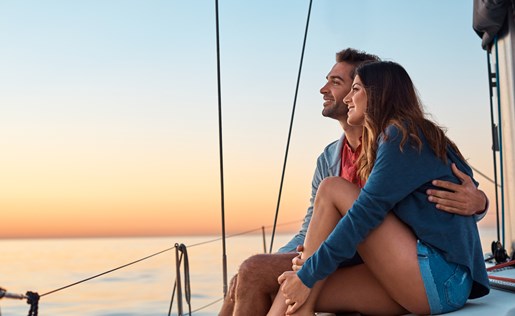Couple hugging, watching a sunset on their sailboat.