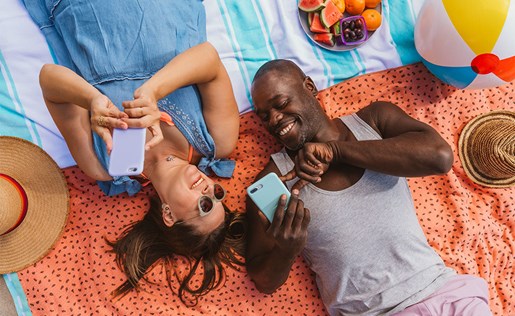 A couple on the beach with their phones splitting a bill